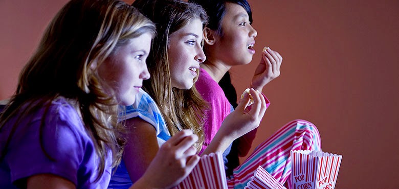three girls eating popcorn and watching a screen