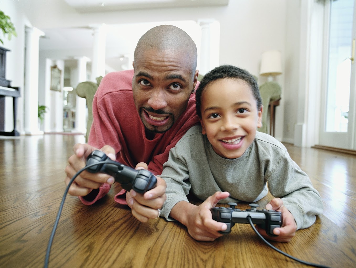 Man and boy playing video games while laying on the floor