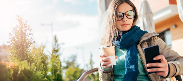 woman drinking coffee in the park while looking at her phone