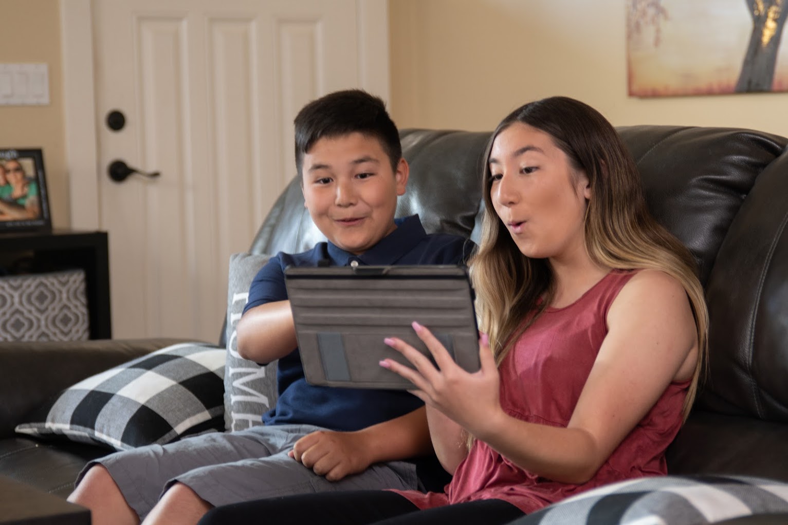 girl and boy sitting on a couch looking at a tablet in girl's hands