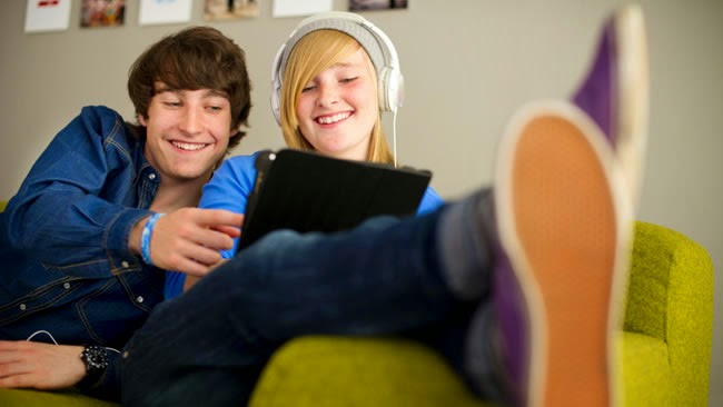 boy and girl sitting on a couch while looking at a tablet